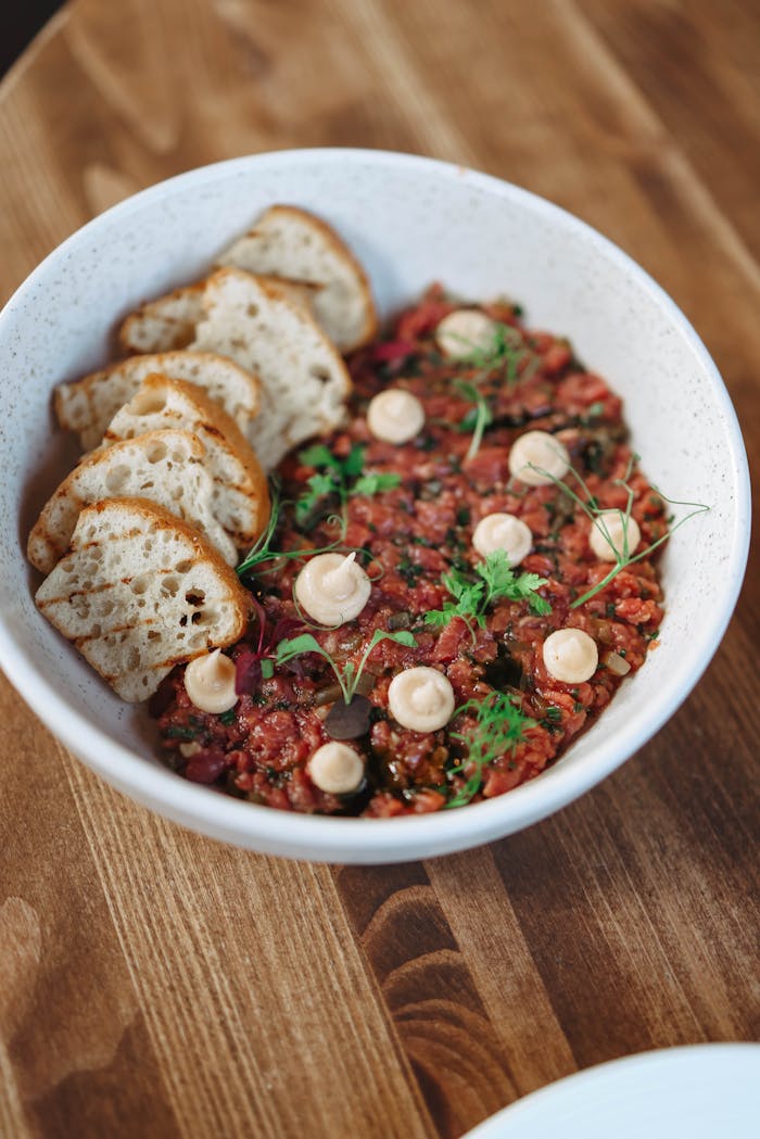 Delicious gourmet tartare served with crisp bread slices in a white bowl on a wooden table.